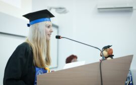 Jeune diplômée en tenue officielle qui prononce un discours debout devant un pupitre