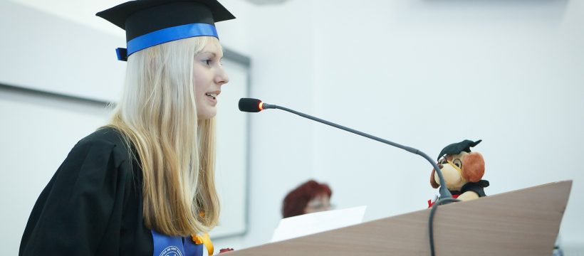 Jeune diplômée en tenue officielle qui prononce un discours debout devant un pupitre