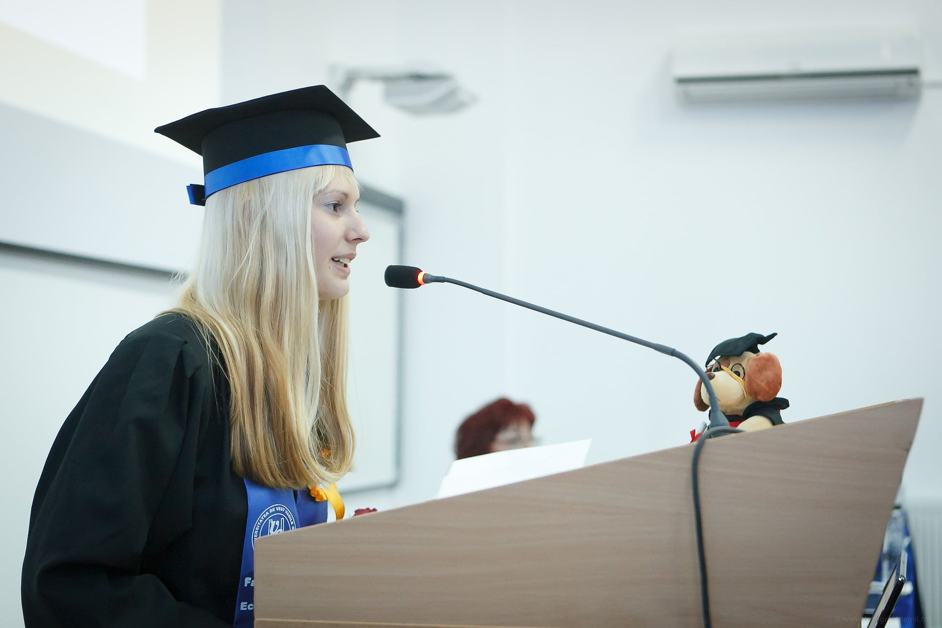 Jeune diplômée en tenue officielle qui prononce un discours debout devant un pupitre